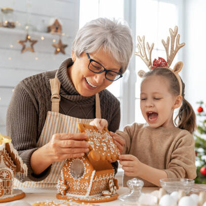 Merry Christmas and Happy Holidays. Family preparation holiday food. Grandmother and granddaughter cooking gingerbread house.